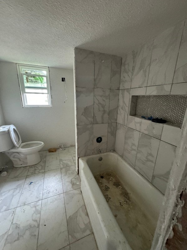 bathroom with tile floors, a textured ceiling, tiled shower / bath, and toilet