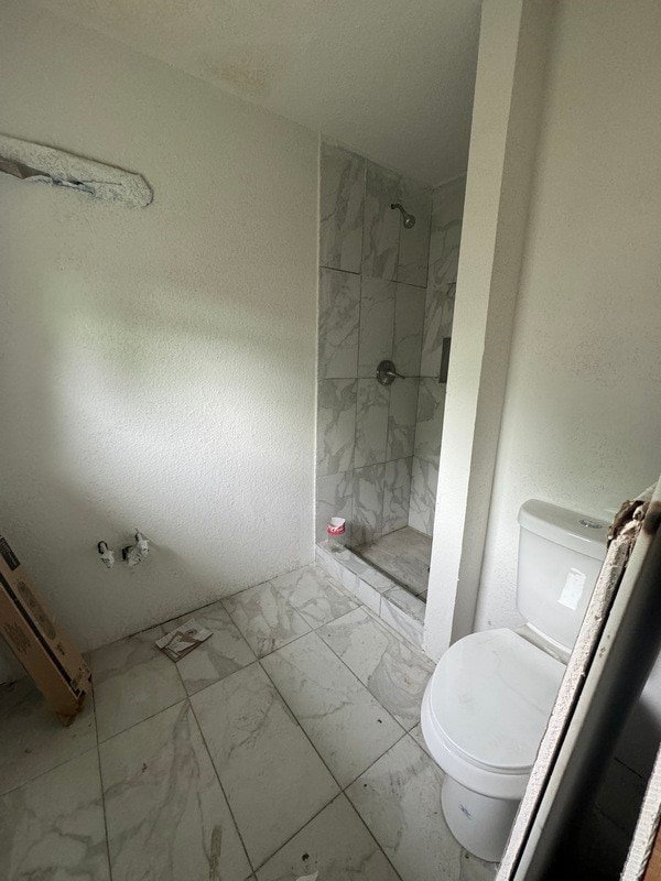 bathroom featuring tile floors, a tile shower, and toilet