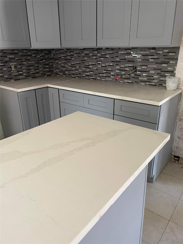 kitchen featuring light stone countertops, gray cabinets, light tile flooring, and tasteful backsplash