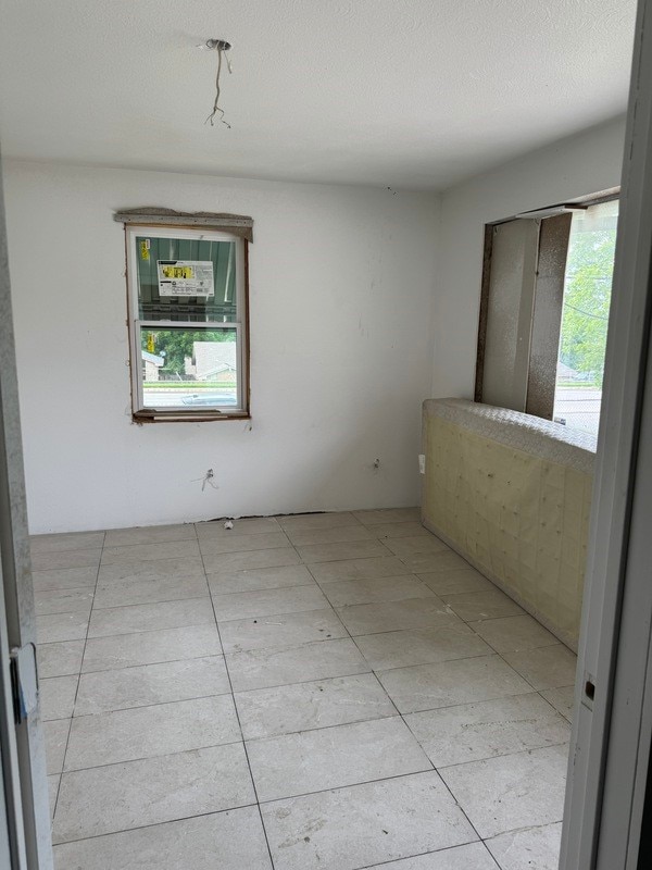 empty room featuring a textured ceiling, a wealth of natural light, and light tile floors