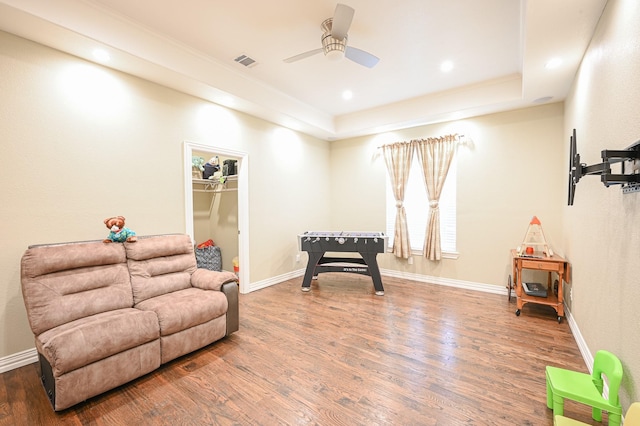 living area featuring a raised ceiling, ceiling fan, and dark wood-type flooring