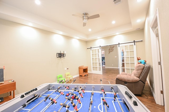 recreation room featuring hardwood / wood-style floors, ceiling fan, a barn door, and a tray ceiling