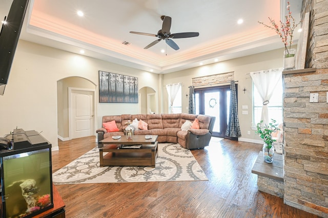 living room with wood-type flooring, a raised ceiling, ceiling fan, and crown molding