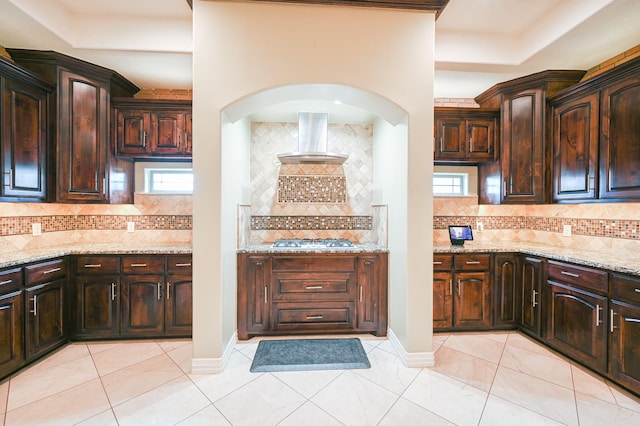 kitchen featuring stainless steel gas stovetop, a healthy amount of sunlight, wall chimney range hood, and tasteful backsplash