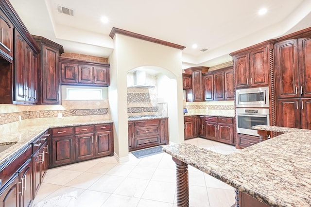 kitchen featuring wall chimney range hood, tasteful backsplash, light tile patterned flooring, light stone counters, and stainless steel appliances