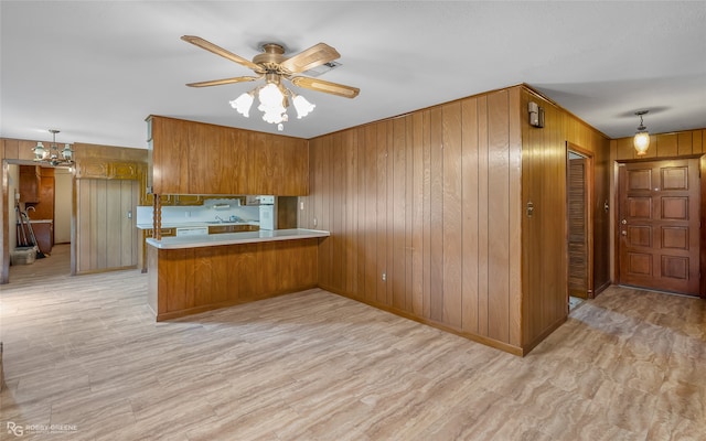 kitchen featuring pendant lighting, wooden walls, kitchen peninsula, and ceiling fan