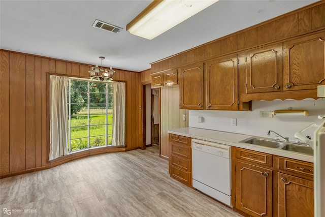 kitchen with decorative light fixtures, an inviting chandelier, wood walls, white dishwasher, and sink