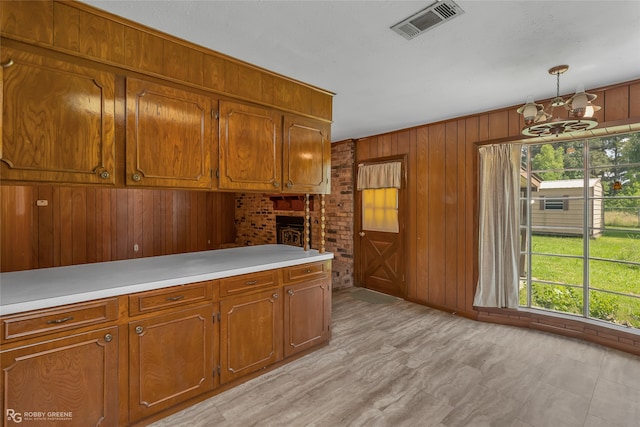 kitchen with a notable chandelier, a brick fireplace, wood walls, and pendant lighting