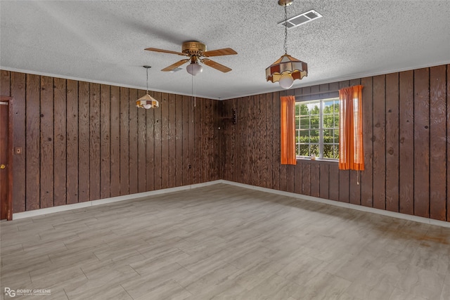 empty room featuring a textured ceiling, ceiling fan, and wood walls