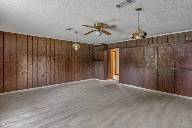 spare room featuring ceiling fan, wooden walls, light hardwood / wood-style flooring, and a textured ceiling