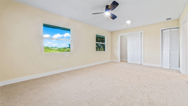 unfurnished bedroom featuring ceiling fan, light carpet, and two closets