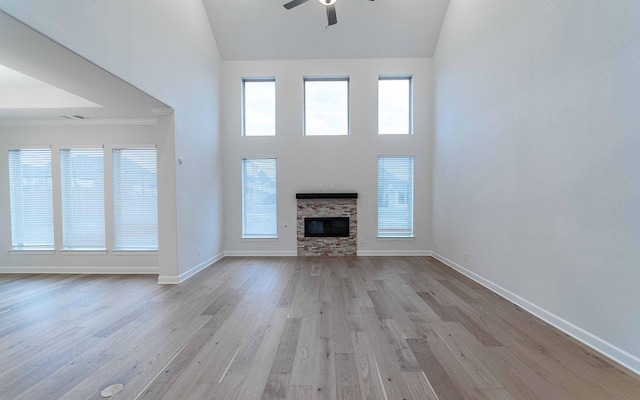 unfurnished living room with ceiling fan, a stone fireplace, high vaulted ceiling, light wood-type flooring, and ornamental molding