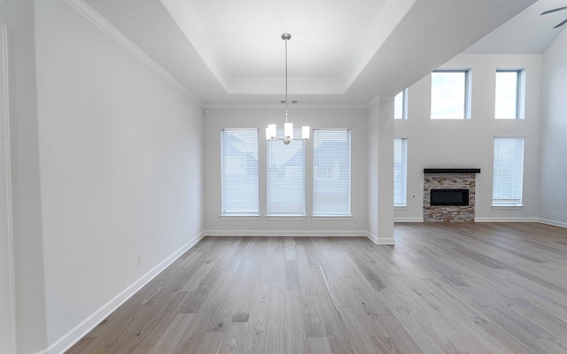 unfurnished living room featuring a raised ceiling, a stone fireplace, light hardwood / wood-style flooring, and ceiling fan with notable chandelier