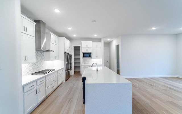 kitchen featuring built in microwave, wall chimney exhaust hood, stainless steel gas cooktop, light hardwood / wood-style floors, and white cabinets