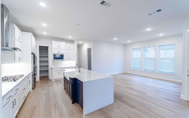 kitchen featuring decorative backsplash, a center island with sink, white cabinetry, and stainless steel appliances