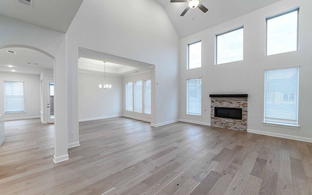 unfurnished living room featuring a towering ceiling, ceiling fan with notable chandelier, light hardwood / wood-style floors, and a stone fireplace