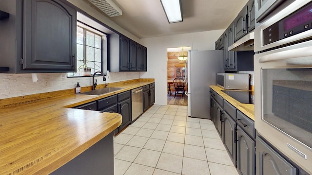 kitchen with appliances with stainless steel finishes, butcher block countertops, light tile patterned floors, and sink