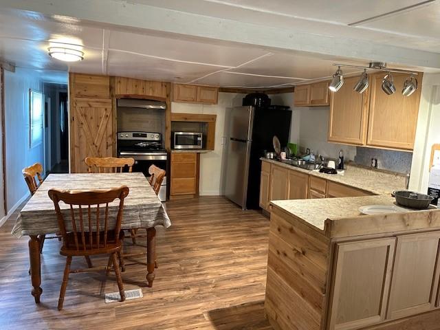 kitchen with wood finished floors, light brown cabinets, a peninsula, light countertops, and appliances with stainless steel finishes