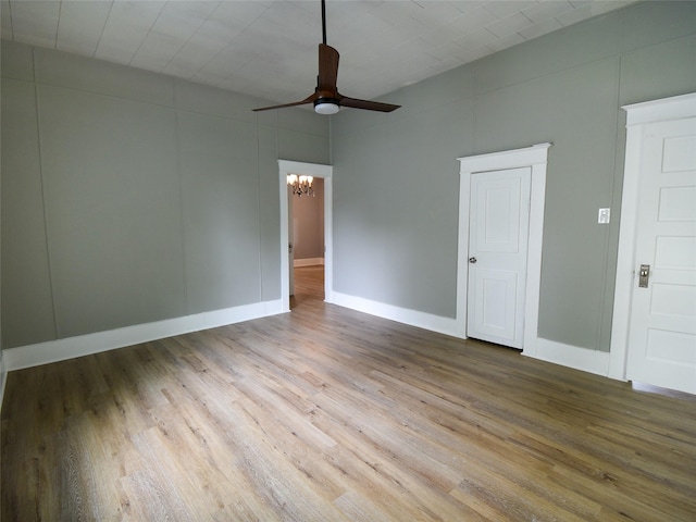 empty room featuring ceiling fan with notable chandelier and light wood-type flooring