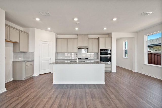 kitchen featuring stainless steel double oven, dark hardwood / wood-style floors, and dark stone counters