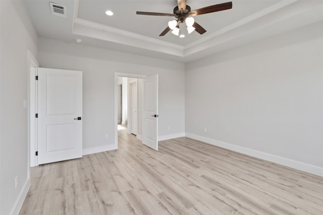 unfurnished bedroom featuring ceiling fan, a tray ceiling, crown molding, and light hardwood / wood-style floors