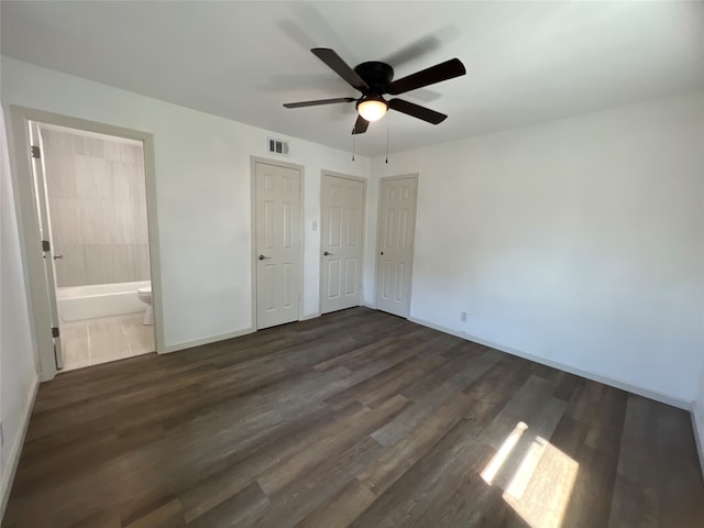 unfurnished bedroom featuring connected bathroom, two closets, dark wood-type flooring, and ceiling fan