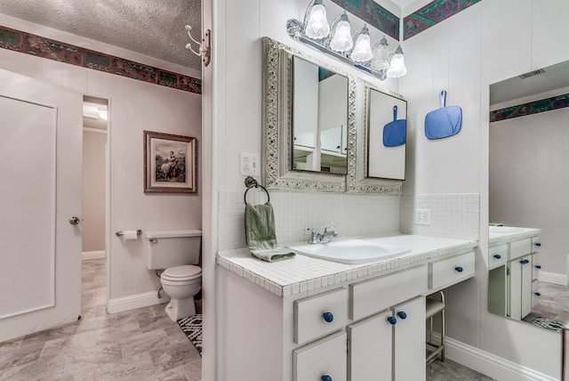 bathroom with a textured ceiling, decorative backsplash, vanity, and toilet