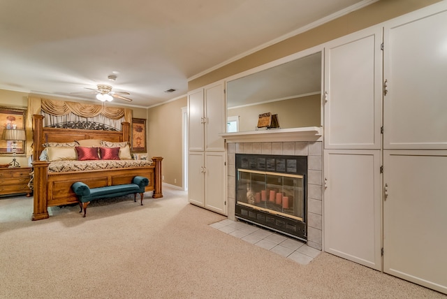 carpeted bedroom featuring a tiled fireplace, ceiling fan, and crown molding