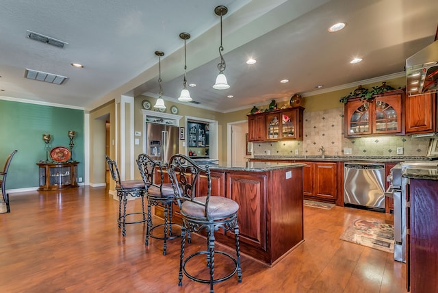 kitchen with dark stone countertops, stainless steel appliances, hanging light fixtures, a center island, and backsplash