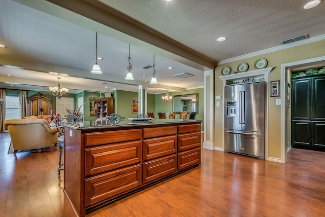 kitchen featuring an inviting chandelier, high quality fridge, pendant lighting, a kitchen island, and a breakfast bar