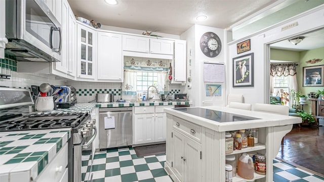 kitchen featuring white cabinets, appliances with stainless steel finishes, a center island, and tile countertops