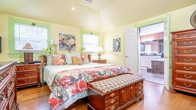 bedroom with connected bathroom, light hardwood / wood-style floors, and lofted ceiling