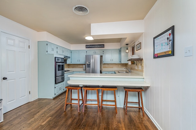 kitchen featuring kitchen peninsula, stainless steel appliances, backsplash, dark wood-type flooring, and sink