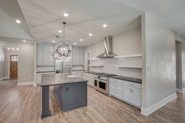 kitchen featuring light hardwood / wood-style flooring, wall chimney range hood, premium appliances, and a kitchen island with sink