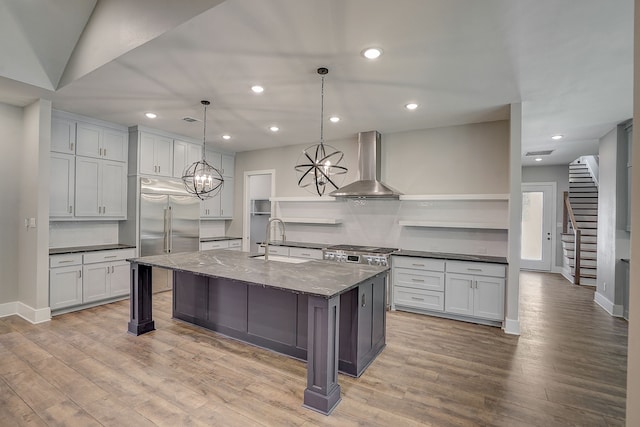 kitchen with light hardwood / wood-style flooring, an island with sink, stainless steel built in refrigerator, wall chimney exhaust hood, and sink