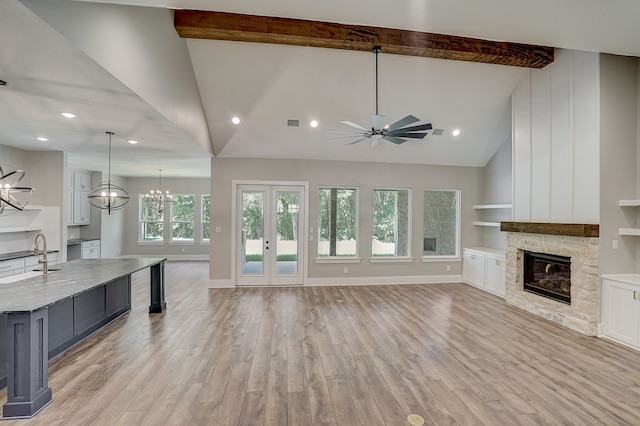 unfurnished living room with beamed ceiling, light hardwood / wood-style floors, a fireplace, and ceiling fan with notable chandelier