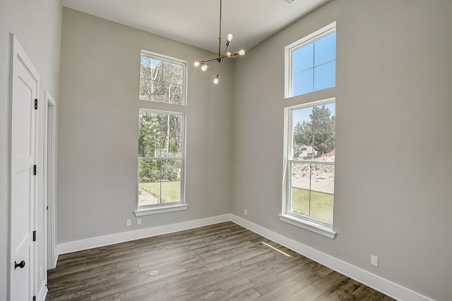 unfurnished room featuring a towering ceiling, an inviting chandelier, and hardwood / wood-style floors