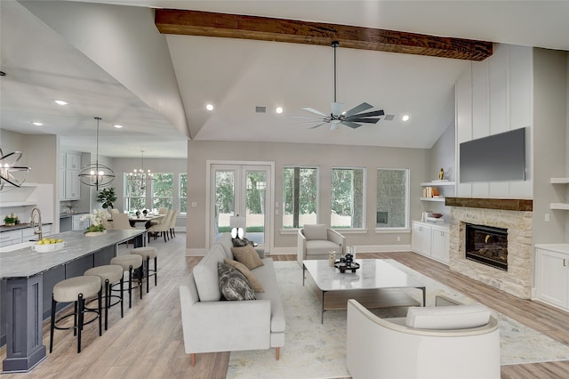 living room with high vaulted ceiling, a stone fireplace, light wood-type flooring, and ceiling fan with notable chandelier