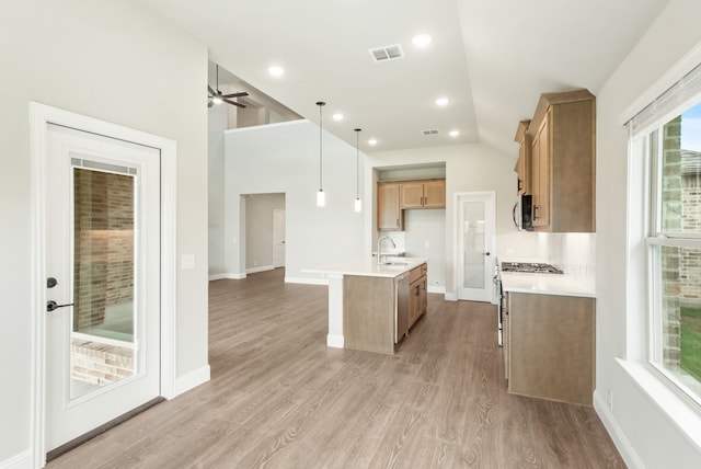 kitchen with decorative light fixtures, light wood-type flooring, sink, ceiling fan, and a center island with sink