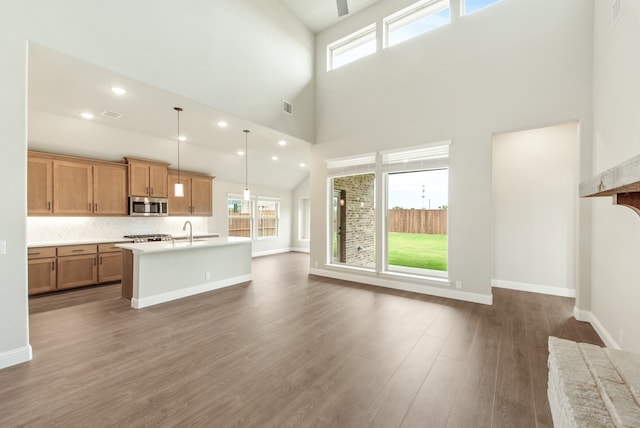 kitchen featuring pendant lighting, high vaulted ceiling, hardwood / wood-style floors, backsplash, and a center island with sink