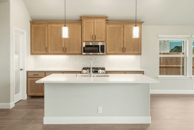 kitchen featuring a kitchen island with sink, light hardwood / wood-style flooring, backsplash, and decorative light fixtures