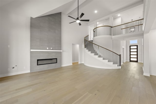 unfurnished living room with high vaulted ceiling, ceiling fan, a tile fireplace, and light hardwood / wood-style floors