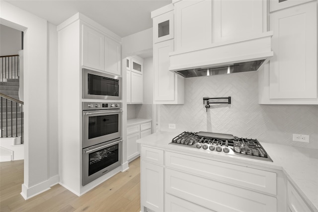 kitchen with appliances with stainless steel finishes, backsplash, white cabinets, and light hardwood / wood-style floors