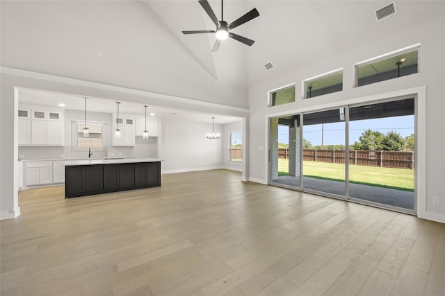 unfurnished living room featuring light hardwood / wood-style flooring, sink, ceiling fan with notable chandelier, and high vaulted ceiling