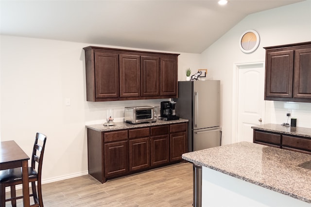 kitchen featuring dark brown cabinetry, lofted ceiling, light wood-type flooring, and stainless steel refrigerator