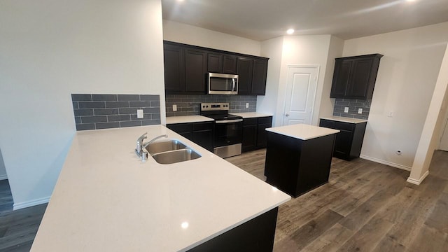 kitchen featuring sink, backsplash, stainless steel appliances, a kitchen island, and dark hardwood / wood-style flooring