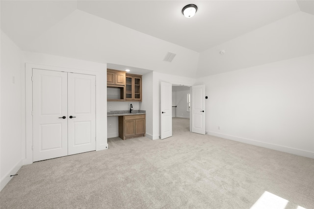 unfurnished bedroom featuring light colored carpet, vaulted ceiling, sink, and a closet