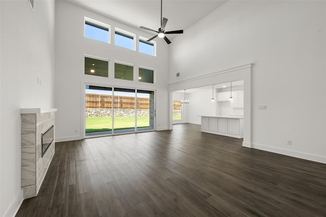 unfurnished living room featuring plenty of natural light, a premium fireplace, ceiling fan, and dark wood-type flooring