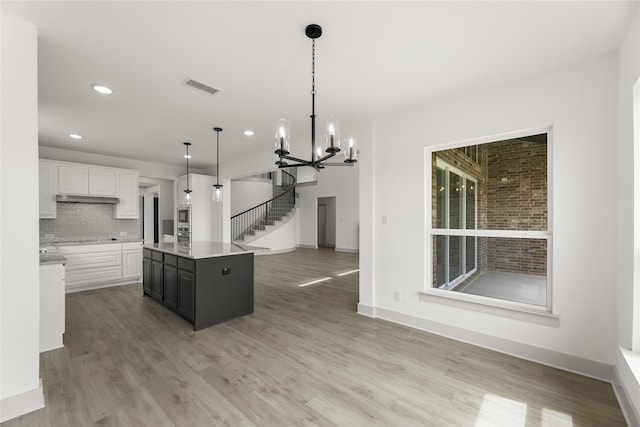 kitchen with a kitchen island with sink, light hardwood / wood-style flooring, decorative light fixtures, decorative backsplash, and white cabinetry