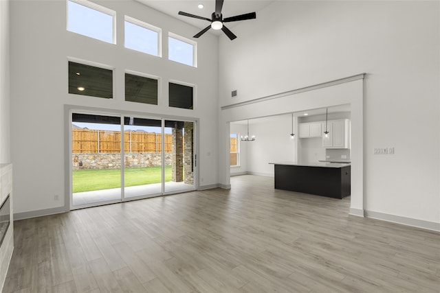 unfurnished living room featuring a high ceiling, plenty of natural light, light hardwood / wood-style floors, and ceiling fan with notable chandelier